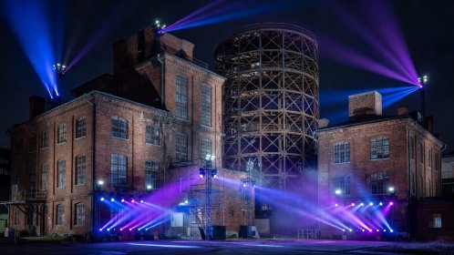 Industrial brick buildings and gas storage tank illuminated by modern festival lighting rigs